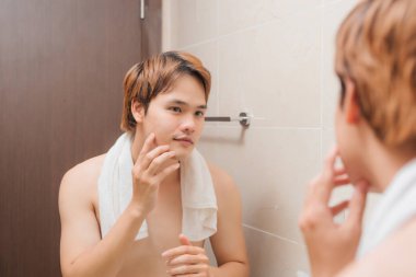 Yakışıklı üstsüz genç adam aynada kendine bakıyor ve yüzüne dokunuyor.