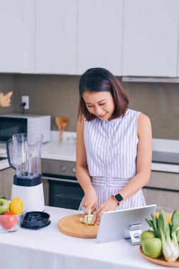 Genç Asyalı kadın tabletten meyve püresi yapıyor.