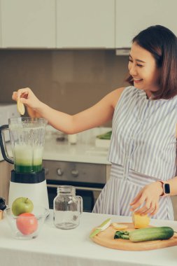 Genç Asyalı kadın mutfakta yeşil smoothie yapmak için blender kullanıyor..