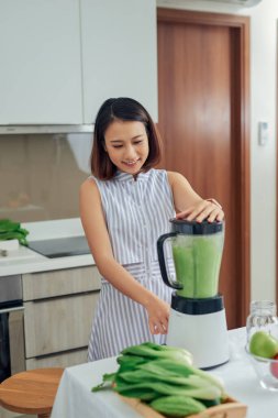 Güzel genç Asyalı kadın mutfakta blender 'da smoothie yapıyor.