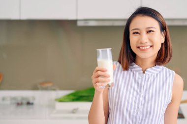 Güzel genç Asyalı kadın evdeki mutfakta süt içiyor..