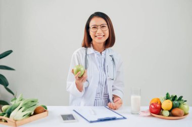 Ofisinde gülümseyen beslenme uzmanı sağlıklı sebzeler, meyveler, sağlık hizmetleri ve diyet konsepti gösteriyor..