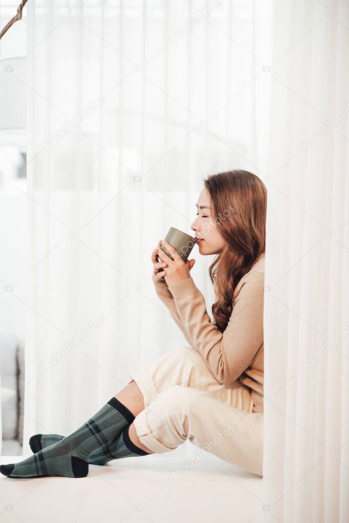 beautiful woman with curled hair is sitting on the window still in a knitted sweater and leg warmers