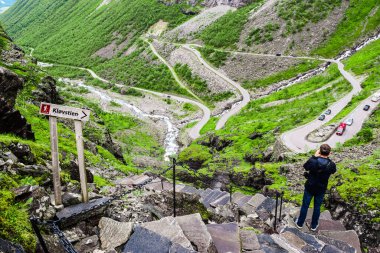 Trollstigen ya da Troll Merdivenleri yakınlarındaki yürüyüş parkurundaki erkek turist, 11 saç tokasından dolayı popüler bir turizm merkezi olan yılansı dağ yolu. Norveç.