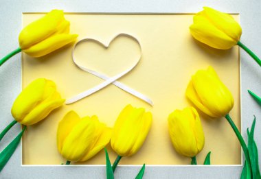 Güneşli sarı bahar çiçek aranjmanı. Sarı kâğıt zemin üzerinde kalbi olan sarı, taze laleler. Kadınlar Günü için tebrik kartı, Anneler Günü, Sevgililer Günü, Aile Günü veya diğer tatiller için. Düz yatıyordu.