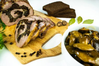 Baharatlar, defne yaprakları, roka ve beyaz bir zemin üzerinde marine edilmiş mantarlı ekmek dilimleriyle süslenmiş bir kesme tahtasında erik ve mantarlı fırında domuz eti..