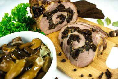 Baharatlar, defne yaprakları, roka ve beyaz bir zemin üzerinde marine edilmiş mantarlı ekmek dilimleriyle süslenmiş bir kesme tahtasında erik ve mantarlı fırında domuz eti..