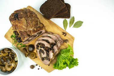 Baharatlar, defne yaprakları, roka ve beyaz bir zemin üzerinde marine edilmiş mantarlı ekmek dilimleriyle süslenmiş bir kesme tahtasında erik ve mantarlı fırında domuz eti..