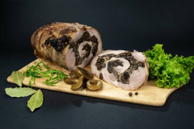 Kuru erik ve mantarlı fırında domuz eti baharatlar, defne yaprakları, roka ve siyah bir zemin üzerinde marine edilmiş mantarlarla süslenmiş bir kesme tahtasının üzerinde parçalara ayrılmış..