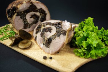 Kuru erik ve mantarlı fırında domuz eti baharatlar, defne yaprakları, roka ve siyah bir zemin üzerinde marine edilmiş mantarlarla süslenmiş bir kesme tahtasının üzerinde parçalara ayrılmış..