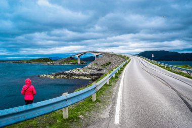 Storseisundet Köprüsü 'nün (Storseisundbrua) arka planındaki kız turist, Atlantik Okyanusu Yolu' nu oluşturan sekiz köprünün en ünlüsü ve en uzunudur. Norveç 'in Ulusal Turizm Rotaları' nın bir parçasıdır..