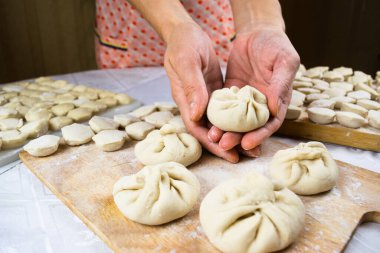 Kadının elleri un kaplı khinkale hamur köftesinin arka planında beyaz bir masaya serpiştirilmiş khinkale mantı, ravioli ve khinkali serpiştirilmiş hamur tatlısı var. Lezzetli ev yemekleri..