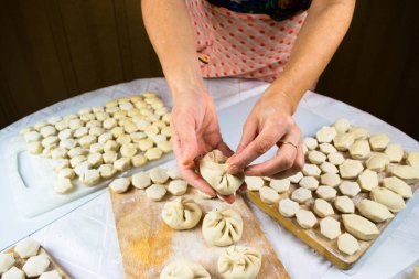 Kadının elleri arka planda khinkale köfteleri yontuyor. Khindi hamuru, ravioli ve khinkali serpiştirilmiş beyaz bir masaya un serpiştiriyor. Lezzetli ev yemekleri..