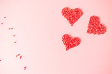 İzole edilmiş açık pembe arka planda aşkın sembolü olarak boncuktan yapılmış üç kırmızı kalp. Sevgililer Günü için tebrik kartı, Anneler Günü ya da diğer tatiller için. Seçici odaklanma. Düz yatıyordu. Boşluğu kopyala.
