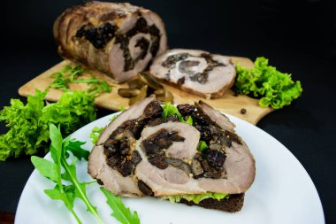 Etli ve otlu sandviç, salata yaprakları ve roka. Siyah arka planda beyaz bir tabakta atıştırmak için. Kuru erik ve mantarlı domuz eti dilimlenmiş tahtada..