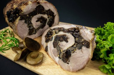 Kuru erik ve mantarlı fırında domuz eti baharatlar, defne yaprakları, roka ve siyah bir zemin üzerinde marine edilmiş mantarlarla süslenmiş bir kesme tahtasının üzerinde parçalara ayrılmış..