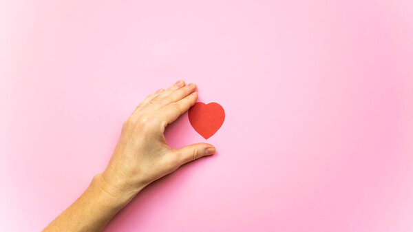 Heart between the fingers of a woman's hand isolated on light pink background. Valentines, Mothers Day or wedding and love concept.