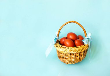 Açık mavi arkaplanda kahverengi Paskalya yumurtalarıyla süslenmiş hasır sepet. Paskalya tebrik kartı. Minimum konsept. Düz yatıyordu. Boşluğu kopyala.