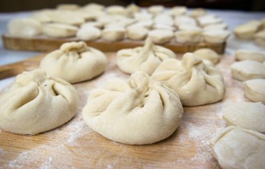 El yapımı khinkali hamur tatlısı ve ravioli kesme tahtasına dizilmiş ve un serpiştirilmiş. Lezzetli ev yapımı yemekler ve hazırlıklar. Yakın çekim, makro.