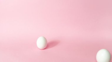 4k Three white chicken eggs dynamically emerge one at a time on light pink background. Happy Easter Day Concept. Greeting card. Stop motion animation. Copy space.
