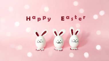 Happy Easter Day. Three cute bunnies made of white chicken eggs isolated on a light pink pastel background. Holiday greeting card with bokeh. Copy space.