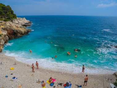Hırvatistan 'ın Pula kenti - 25 Haziran 2019: Adriyatik Denizi' nin serbest taşlı ve çakıl taşı plajında tatilciler güneşli bir yaz gününde. Verudela tatil kompleksi. Harika bir deniz uykusu.