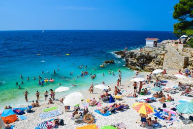 Hırvatistan 'ın Pula kenti - 25 Haziran 2019: Adriyatik Denizi' nin serbest taşlı ve çakıl taşı plajında tatilciler güneşli bir yaz gününde. Verudela tatil kompleksi. Harika bir deniz uykusu.