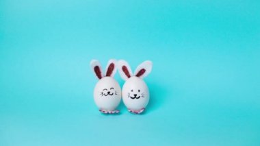 4k Beyaz Tavuk yumurtasından yapılmış iki şirin Paskalya tavşanı hareketi ve tatil için tebrikler. Mutlu Paskalya Tavşanı Günü Kavramı. Açık mavi arkaplan. Tatil tebrik kartı. Hareket animasyonunu durdur. Boşluğu kopyala.