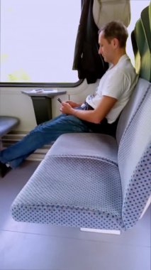 Bir adam akıllı telefonunu tutarak trene biniyor. Yolcu kamusal alanlarda sosyal mesafeyi korumak için iki sıra halinde tek başına oturuyor. Minsk yolu, Brest. Beyaz Rusya. Dikey video.