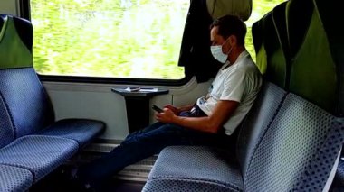 Koruyucu maske takan erkek yolcu trene biniyor. Yolcu kamusal alanlarda sosyal mesafeyi korumak için iki sıra halinde tek başına oturuyor. Minsk yolu, Brest. Beyaz Rusya.