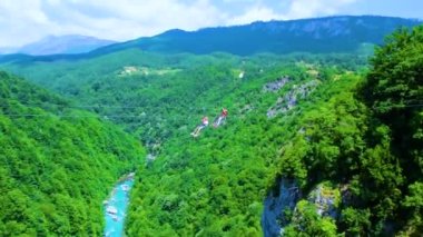Turist, Tara Nehri Kanyonu ya da yüksek dağlar arasındaki Tara Nehri Vadisi üzerinde bir halatla kayar. Kanyon Avrupa 'daki en büyük ve en derin kanyondur. Durdevica Tara Köprüsü 'nden görüntü. Karadağ.