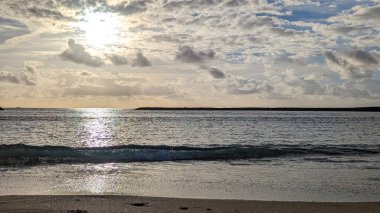 Güzel gün batımı. Sakin Atlantik Okyanusu 'nun üzerindeki beyaz bulutların arasından güneş ışınları. Kumlu sahilde sörf dalgaları. Playa de las Americas plajı, Tenerife, Kanarya Adaları. İspanya.