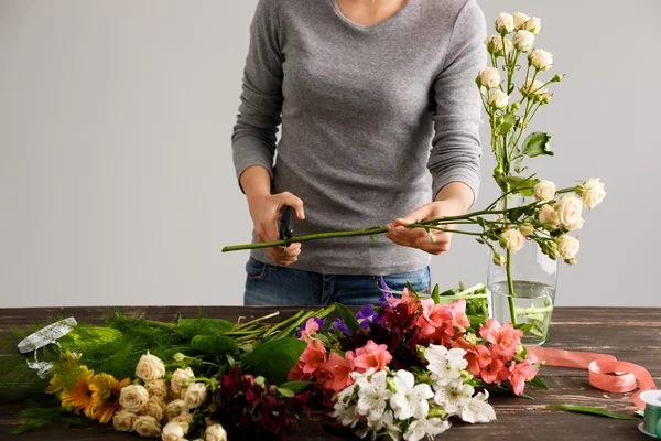 Girl  make a bouquet over gray background, cutting stem.