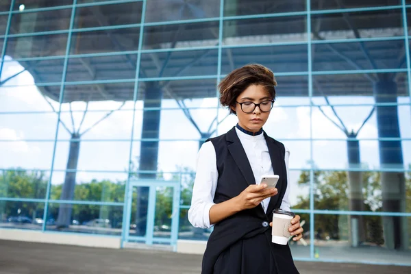 Young successful businesswoman looking at phone, standing near business centre.