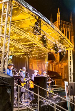 Worcestershire, İngiltere-29 Kasım 2024: Yerel bir grup, Katedral meydanında kurulmuş geçici bir sahnede, akşam saatlerinde tarihi bir dönüm noktasının karşısında Noel 'e kadar sahne alıyor..