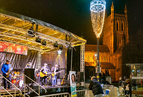 Worcestershire,England-November 29 2024: A local band plays on a temporary stage set up, in Cathedral square,opposite the historic landmark in the early evening,during the build up to Christmas.