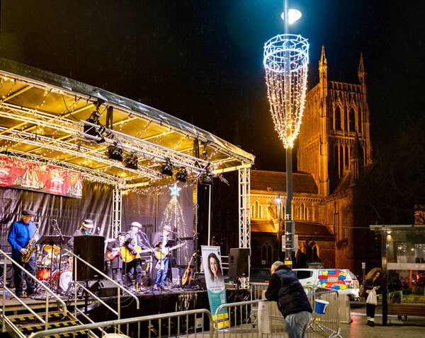 Worcestershire,England-November 29 2024: A local band plays on a temporary stage set up, in Cathedral square,opposite the historic landmark in the early evening,during the build up to Christmas.