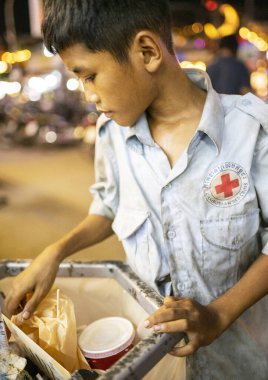 Siem Reap, Kamboçya-02 Nisan 2025: Şehrin sokaklarında, fakir genç bir çocuk, halka açık bir çöp toplama konteynırında değerli eşyalar arıyor..