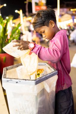 Siem Reap, Kamboçya-Nisan 02 2025: Şehir merkezinde, fakir bir genç ya da 'sokak çocuğu' umumi bir çöp ve çöp torbasında değerli olabilecek eşyalar arıyor.