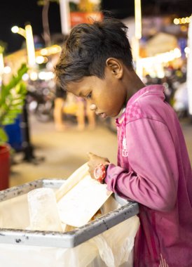 Siem Reap, Kamboçya-Nisan 02 2025: Şehir merkezinde, fakir bir genç ya da 'sokak çocuğu' umumi bir çöp ve çöp torbasında değerli olabilecek eşyalar arıyor.