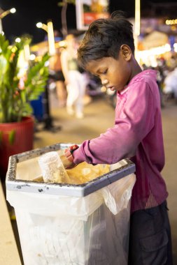 Siem Reap, Kamboçya-Nisan 02 2025: Şehir merkezinde, fakir bir genç ya da 'sokak çocuğu' umumi bir çöp ve çöp torbasında değerli olabilecek eşyalar arıyor.