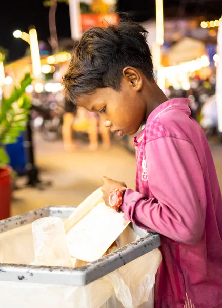 Siem Reap, Kamboçya-Nisan 02 2025: Şehir merkezinde, fakir bir genç ya da 'sokak çocuğu' umumi bir çöp ve çöp torbasında değerli olabilecek eşyalar arıyor.