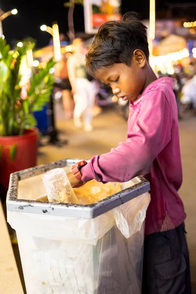 Siem Reap, Kamboçya-Nisan 02 2025: Şehir merkezinde, fakir bir genç ya da 'sokak çocuğu' umumi bir çöp ve çöp torbasında değerli olabilecek eşyalar arıyor.