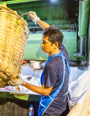 Bangkok, Tayland-26 Nisan 2025: Belediye çöp toplayıcıları, yerel dükkanlar ve evlerin çöpleriyle dolu bambu sepetlerini, bekleyen bir çöp arabasının arkasındaki makineler tarafından ezilmek üzere atıyorlar.