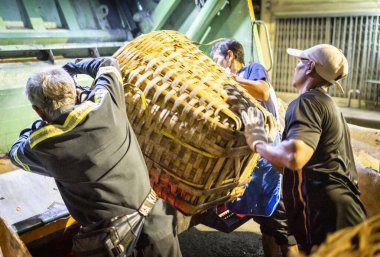 Bangkok, Tayland-26 Nisan 2025: Belediye çöp toplayıcıları, yerel dükkanlar ve evlerin çöpleriyle dolu bambu sepetlerini, bekleyen bir çöp arabasının arkasındaki makineler tarafından ezilmek üzere atıyorlar.