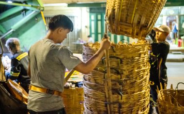 Bangkok, Tayland-26 Nisan 2025: Belediye çöp toplayıcıları, yerel dükkanlar ve evlerin çöpleriyle dolu bambu sepetlerini, bekleyen bir çöp arabasının arkasındaki makineler tarafından ezilmek üzere atıyorlar.