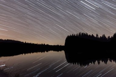 Bir gölün önündeki yıldızlı bir gecede, Almanya 'da, gölde yansımaları olan yıldız izleri.