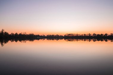 Sarchinger Weiher kıyıları ile manzara ve gün batımı bulutsuz güzel renklerin oynadığı pürüzsüz gölde gökyüzünün yansıması, Almanya