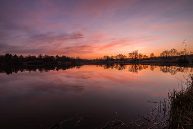 Regensburg 'daki Westpark Donaupark sahilinde manzara ve gün batımı. Pürüzsüz gölde gökyüzünün yansıması. Renklerin güzel dramatik oyunu bulutlarla oynuyor.
