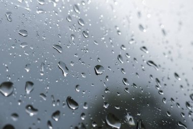 Üzücü, melankolik pencere camına düşen yağmur damlalarının görüntüsü. Yoğunlaşmalı gri, soyut arkaplan fırtınalı havada kasvetli duygular yaratıyor.